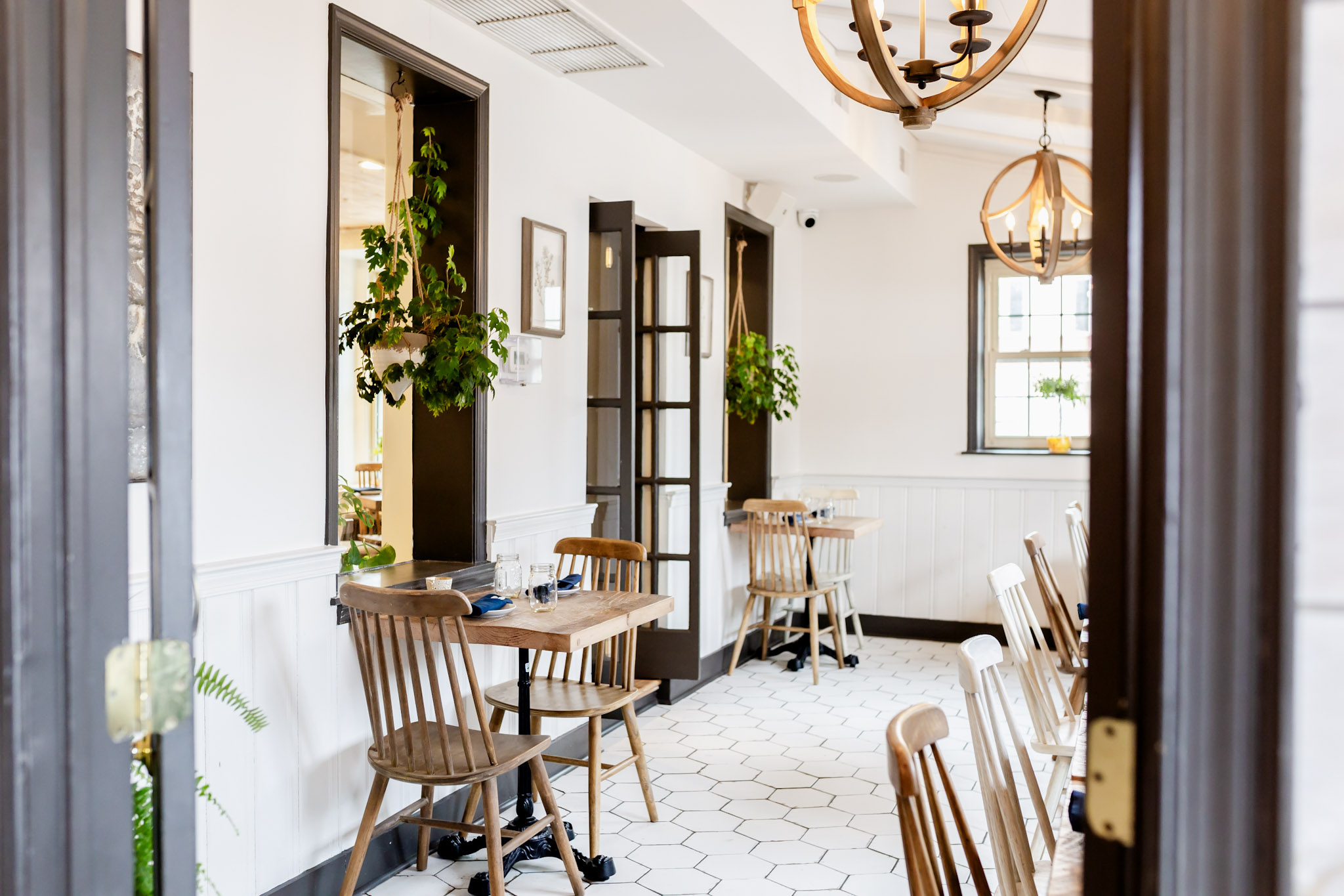 Sunlit dining room with wood tables, spindle chairs and hanging plants at Bloom Southern Kitchen